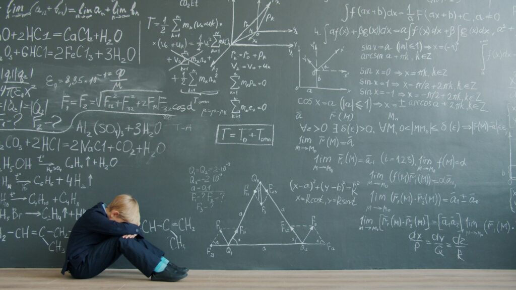 Sylwetka nauczyciela siedzącego pod tablicą pełną formuł matematycznych